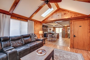 A spacious living room with a leather sofa, wooden dining table, and a ceiling fan.