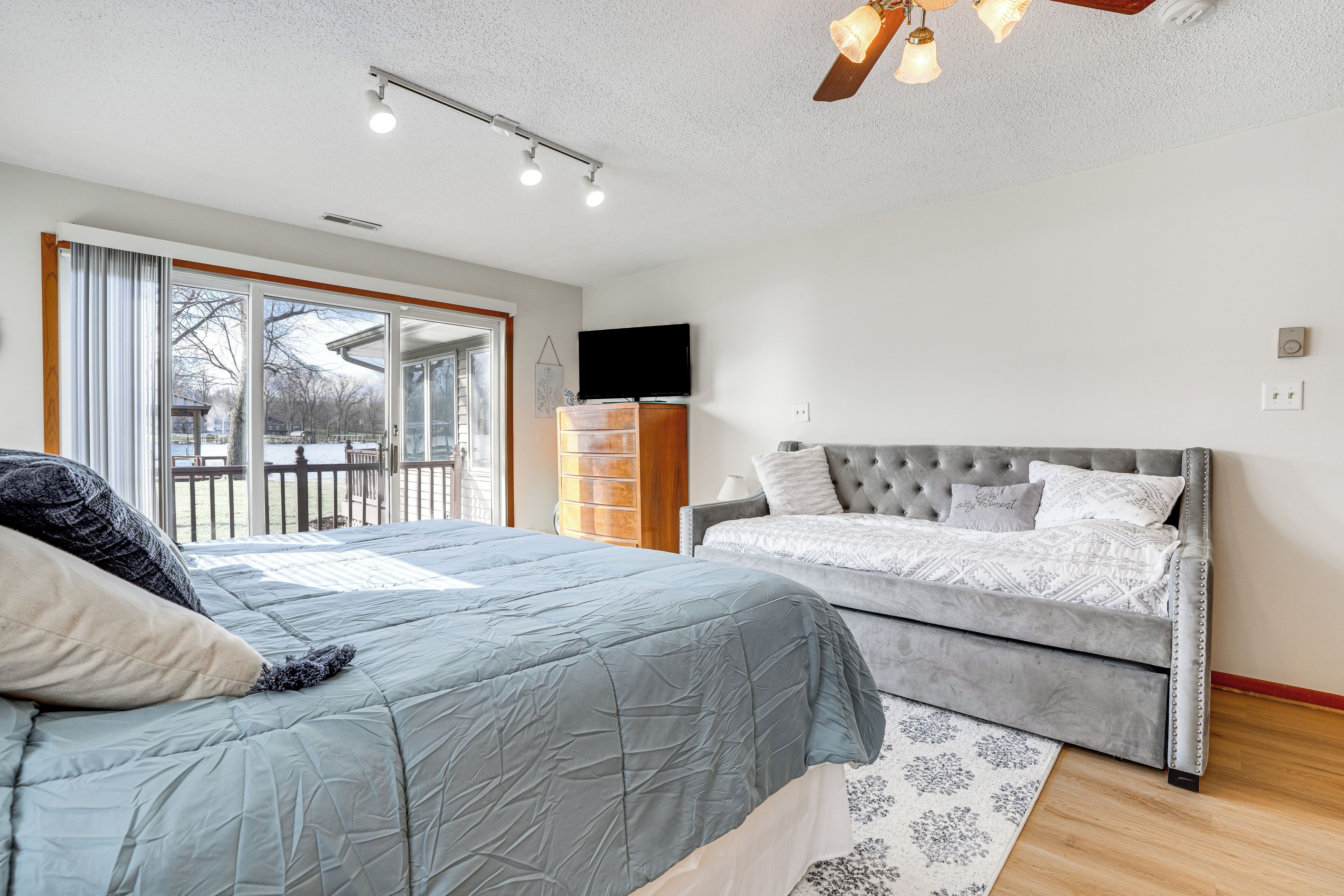 A bedroom with a large bed, a smaller sofa, a television, and a view of the outdoors.