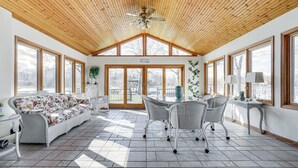Une pièce spacieuse avec un haut plafond en bois, de grandes fenêtres, un canapé blanc, une table à manger avec des chaises et un ventilateur de plafond.