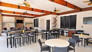 A spacious outdoor dining area with multiple tables and chairs, a stone fireplace, and a bar area with a television. - Beautiful 5 Bed Pool Home With Game Room 5 Bedroom Home by RedAwning (Davenport)