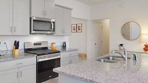 A modern kitchen with white cabinets, stainless steel appliances, granite countertops, and a large island with a sink. - Beautiful 5 Bed Pool Home With Game Room 5 Bedroom Home by RedAwning (Davenport)