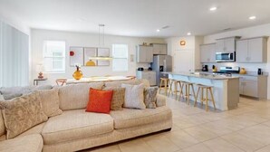 A modern kitchen with a central island, bar stools, and a dining area with a sofa. - Beautiful 5 Bed Pool Home With Game Room 5 Bedroom Home by RedAwning (Davenport)