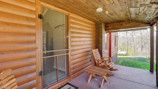 A log cabin with a porch, wooden chairs, and a welcome mat.