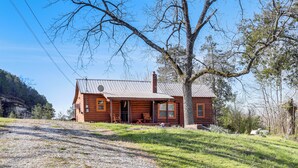 A rustic log cabin with a porch, a chimney, and a gravel driveway.