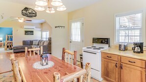 A cozy kitchen with a wooden dining table, chairs, and a stove. There is a sofa and a small dining table in the background.