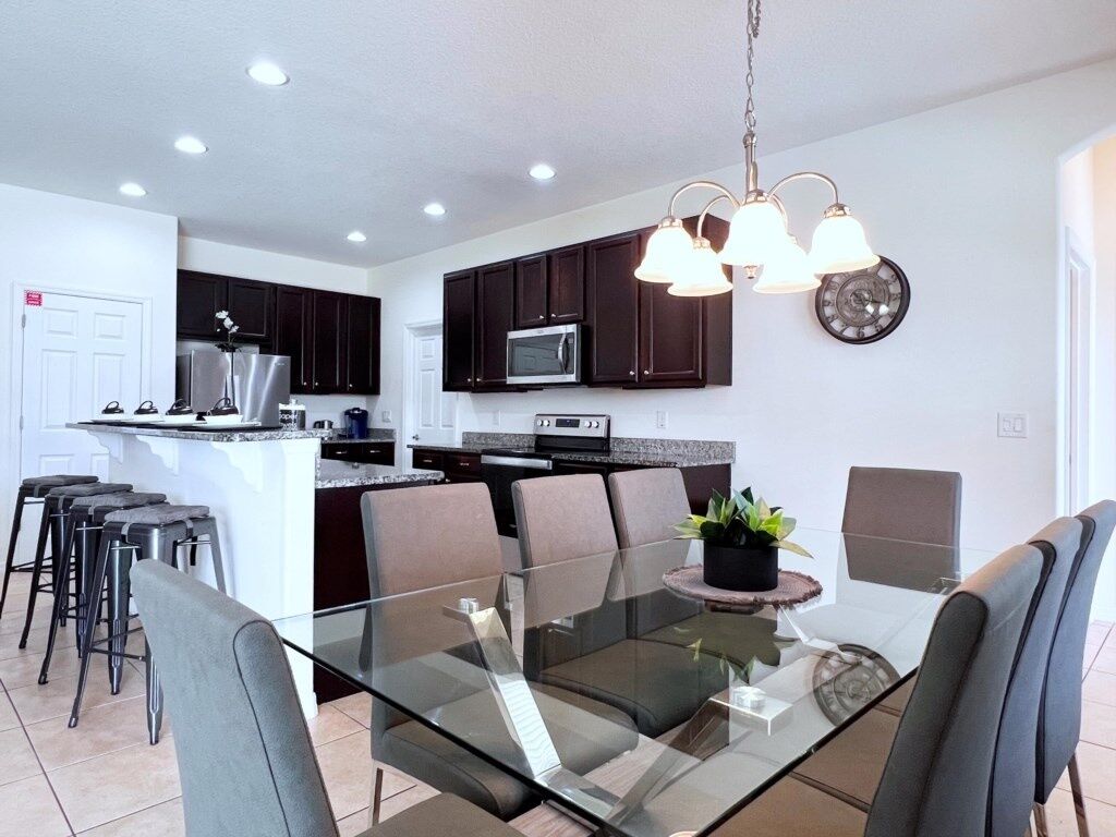 A modern kitchen with dark cabinets, a central island, and a dining area with a glass table and chairs.