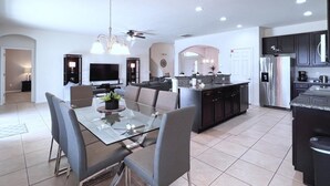 A modern kitchen with a dining area, featuring a large island, dark cabinetry, and a built-in oven. - Cozy Family Friendly Pool Home With Game Room 5 Bedroom Home by RedAwning (Davenport)