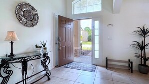 A well-lit entrance with a glass table, decorative wall piece, and a bench. - Cozy Family Friendly Pool Home With Game Room 5 Bedroom Home by RedAwning (Davenport)