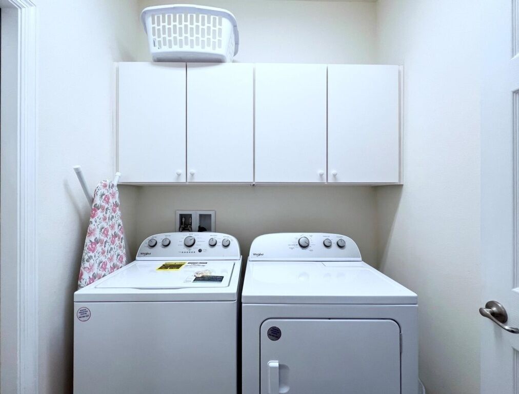 A laundry room with two stacked washers and dryers, a basket on the wall, and a door to the right.