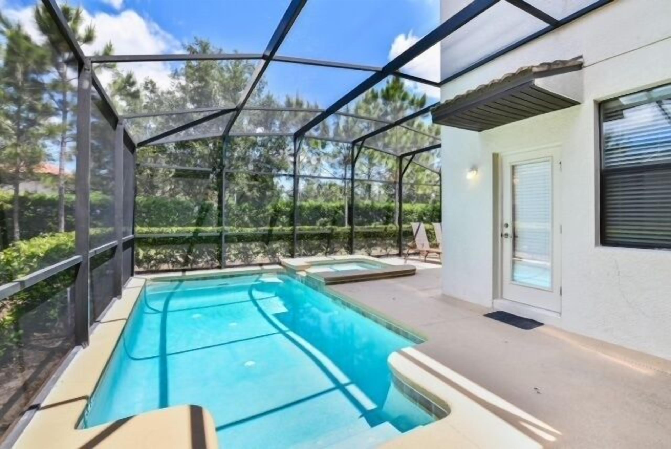 A covered outdoor swimming pool with a glass enclosure, adjacent to a white building with a door and window.