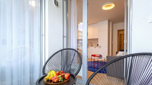 Varanda com mesa, frutas, duas cadeiras de vime e vista para uma cozinha e sala de estar modernas.