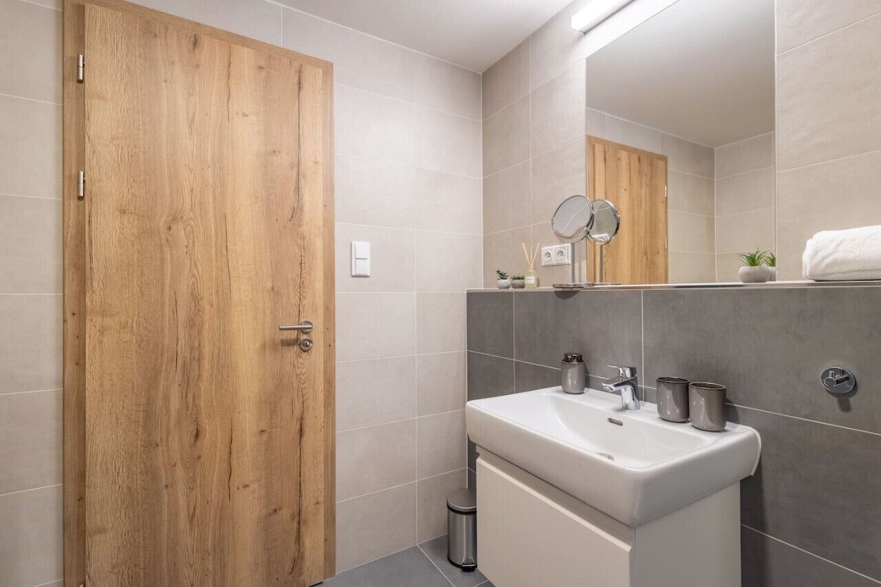 A modern bathroom with a wooden door, a white sink, and a mirror.