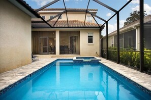 A swimming pool with a glass enclosure, a covered patio, and a view of a house with a tiled roof. - Beautiful 5 Bed Pool Home In Reunion 5 Bedroom Home by RedAwning (Kissimmee)