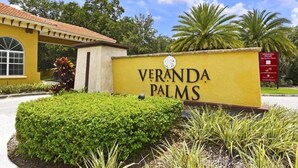 Un cartello giallo con su scritto "VERANDA PALMS", circondato da vegetazione e palme.