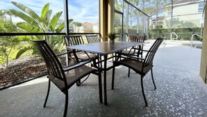 Een overdekt terras met een tafel en stoelen, grote ramen en uitzicht op de omgeving.