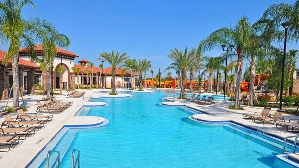 Een groot buitenzwembad met meerdere banen, omringd door palmbomen en ligbedden.