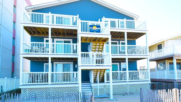 A multi-story hotel with balconies, a sign indicating it is an oceanfront property, and a wooden fence in front. - Ocean Manor 1n 3 Bedroom Condo by RedAwning (Ocean City)