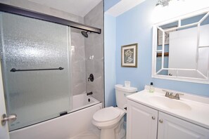 A bathroom with a glass-enclosed shower, a toilet, a sink with a mirror, and a framed artwork on the wall. - Seabay Vista II 102 2 Bedroom Condo by RedAwning (Ocean City)
