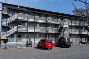 A multi-story motel with balconies, a fire escape, and a parking area with two cars. - Seabay Vista II 102 2 Bedroom Condo by RedAwning (Ocean City)