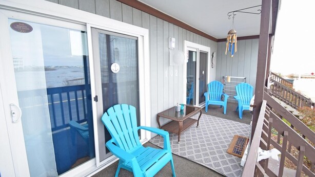 A balcony with blue Adirondack chairs, a glass door, and a small table. - Seabay Vista II 102 2 Bedroom Condo by RedAwning (Ocean City)