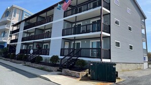 A multi-story building with balconies, a flag, and a stairway leading to the entrance. - Seabay Vista II 102 2 Bedroom Condo by RedAwning (Ocean City)