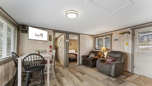 A room with a dining table, chairs, a sofa, and a TV mounted on the wall. - Gone Fishin 2 Bedroom Cabin by RedAwning (Kimberling City)