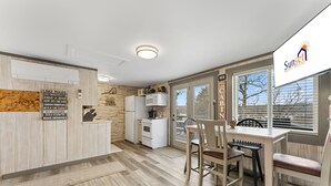 A modern kitchen with white appliances, a dining area with wooden chairs, and a large window offering a view of the outdoors. - Gone Fishin 2 Bedroom Cabin by RedAwning (Kimberling City)