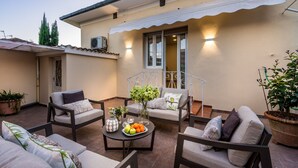 A sunlit patio with outdoor seating, a potted plant, and a table with fruits and a vase. - Casa Lavinia in Lucca (Lucca)