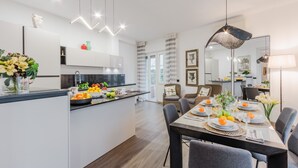 A modern kitchen with a central island, dining area with a long table, and a living space with a sofa and chairs. - Casa Lavinia in Lucca (Lucca)