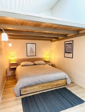 Une chambre à coucher comprenant un lit, une tête de lit en bois, deux lampes fixées au mur et deux œuvres d’art encadrées.