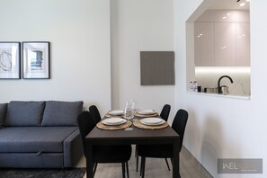 Un salon moderne avec un canapé gris, une table à manger dressée avec des assiettes et des verres, et un coin cuisine équipé de placards et d’un évier.