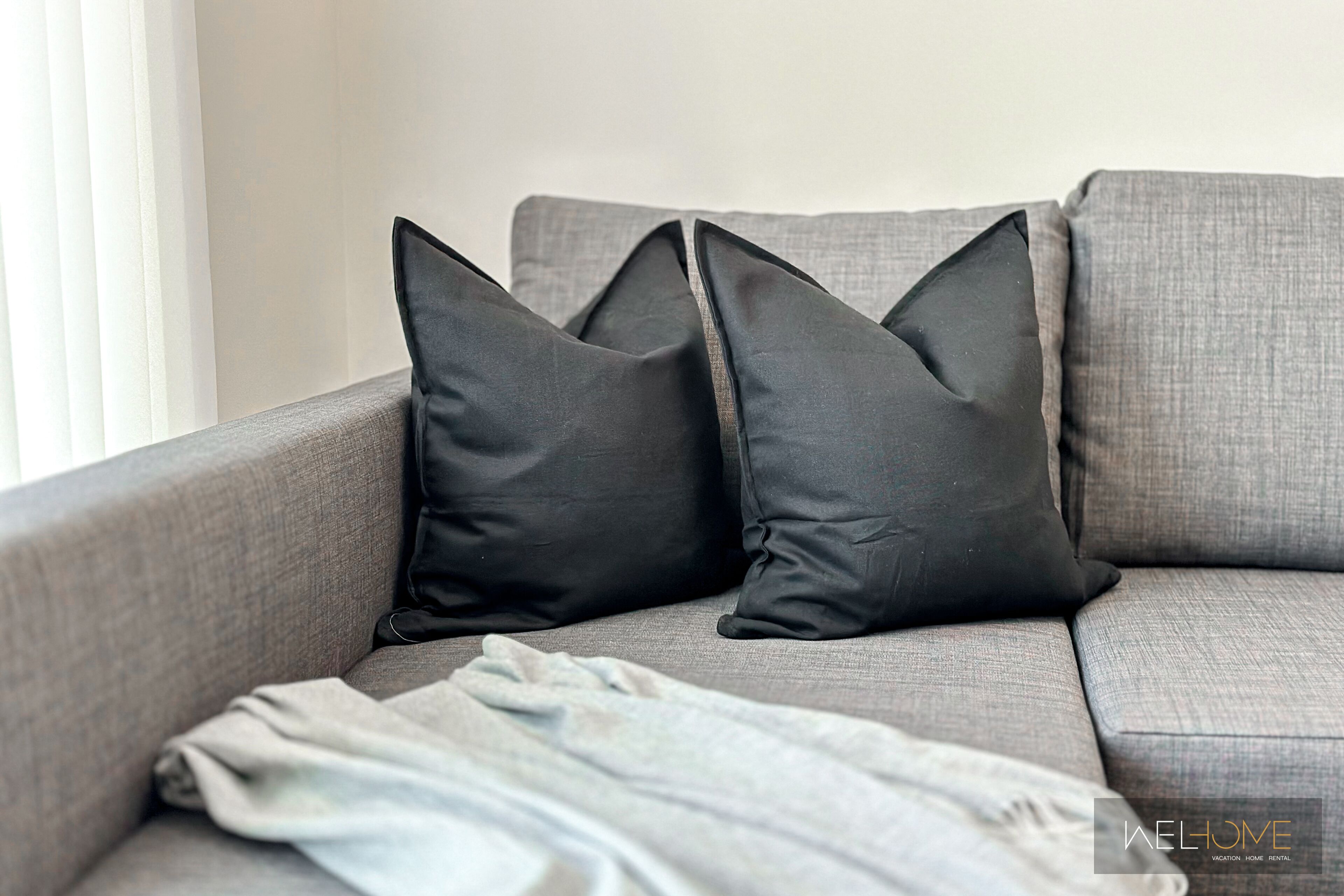 A grey sofa with two black pillows and a light grey throw blanket.