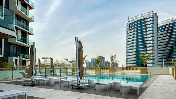 A rooftop pool area with sun loungers and umbrellas, surrounded by modern buildings.