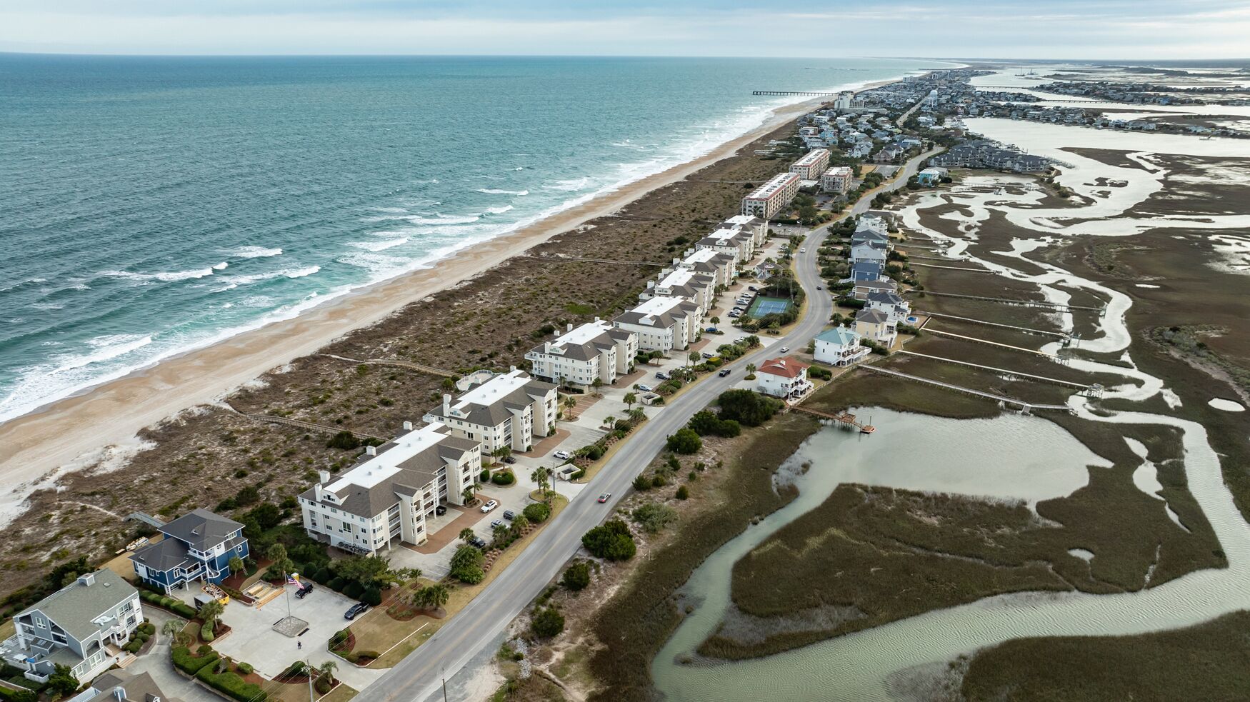 An aerial view of a coastal residential area with beachfront properties, roads, and a pier.