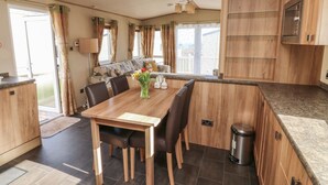 A modern kitchen with wooden cabinets, a dining table with chairs, and a view to the outside. - A La Mer (Paignton)