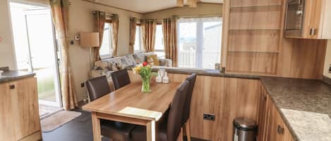 A modern kitchen with wooden cabinets, a dining table with chairs, and a view to the outside.