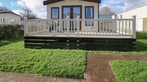 A mobile home with a white exterior, a covered porch, and a small deck. - A La Mer (Paignton)