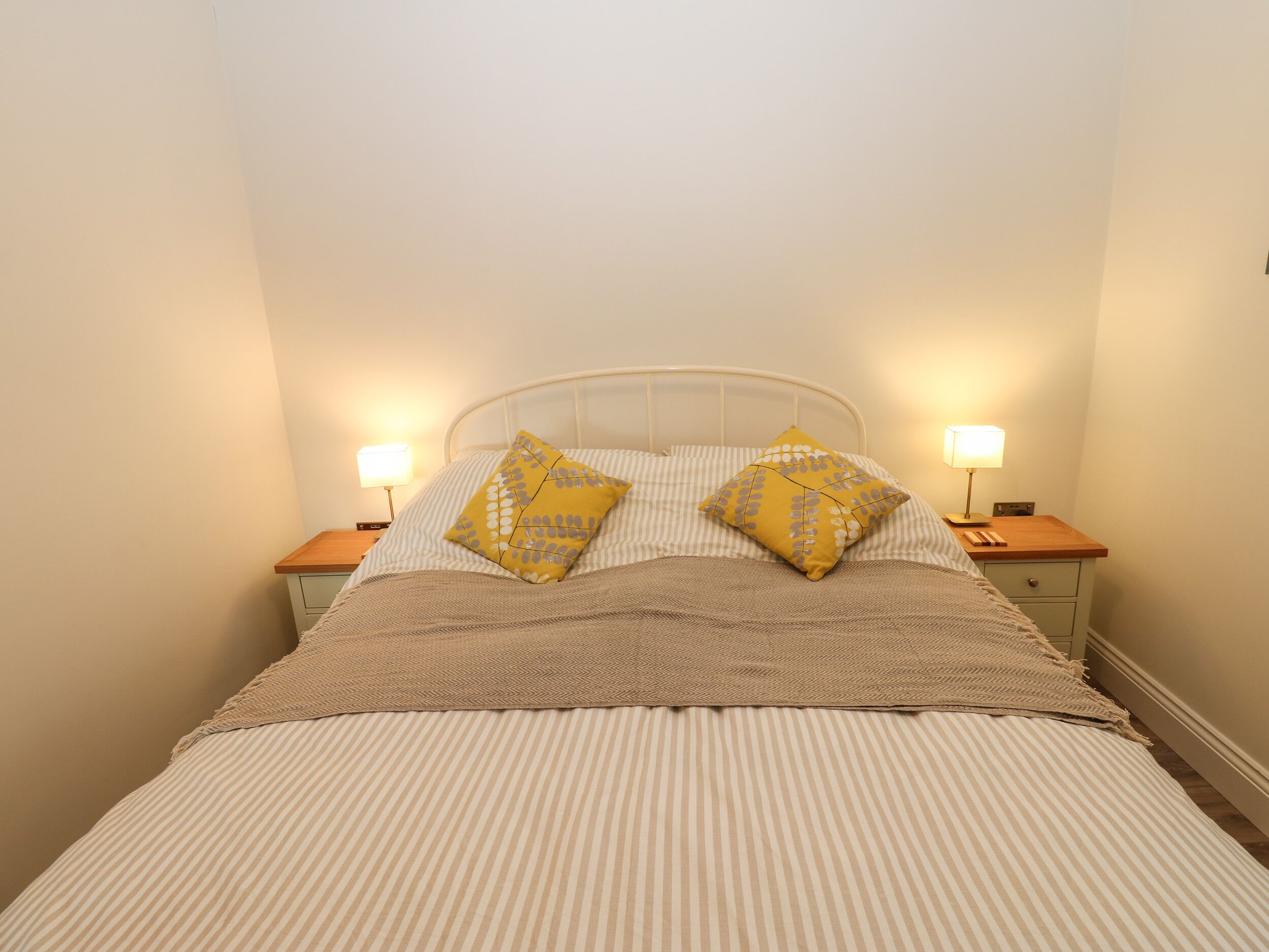 A bed with striped bedding, two pillows, two bedside lamps, and a wooden nightstand.