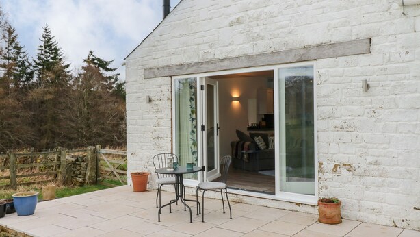 A white brick house with a patio, a table, and chairs. - The Barn (Bishop Auckland)