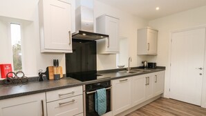 A modern kitchen with white cabinetry, a black range hood, a stainless steel sink, and a wooden countertop. - The Barn (Bishop Auckland)
