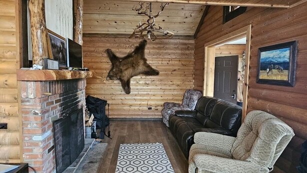 L’intérieur d’une cabane en rondins, avec une cheminée, un canapé en cuir et une tête d’animal empaillée accrochée au mur.