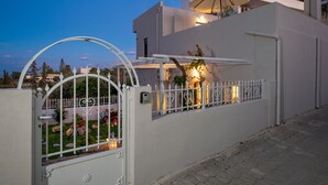 Una casa moderna con fachada blanca, entrada protegida por una reja y un pequeño jardín visible a través de ella.