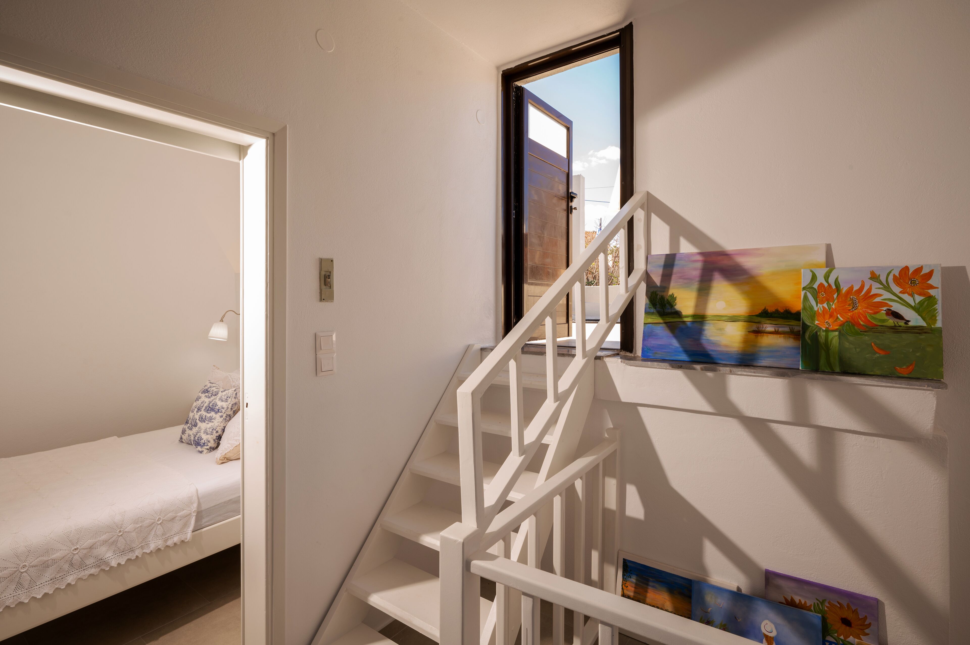 A bedroom with a single bed, a white staircase, and a wall with paintings.