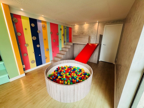 Un espace de jeux avec une piscine à balles, des panneaux muraux colorés et un escalier en bois.