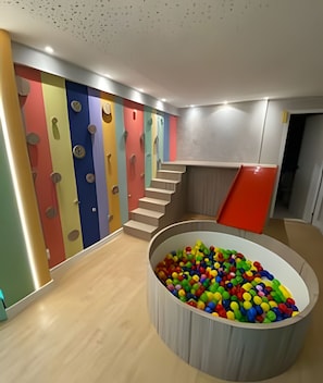 Un espace de jeux pour enfants avec des murs d’escalade colorés, une piscine à balles et un escalier.