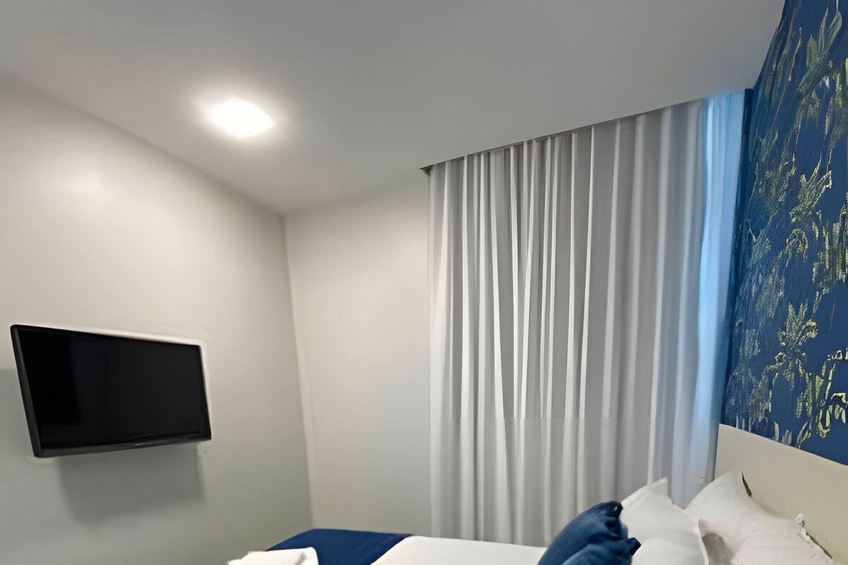 Habitación de hotel con cama, televisión de pantalla plana, ventana con cortinas y una obra de arte colgada en la pared.