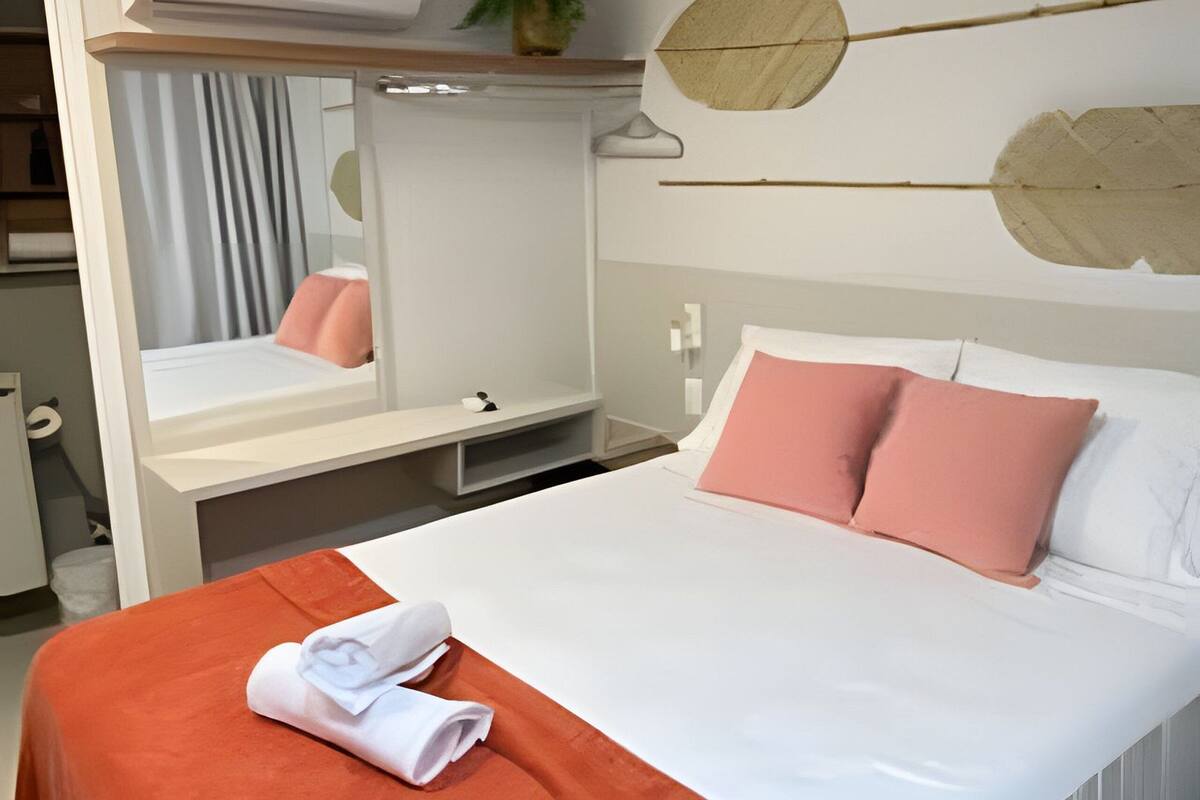 Una habitación de hotel con cama, escritorio, espejo y aire acondicionado.