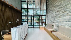 A reception area with a marble counter, wooden paneling, a seating area with a sofa, and a view through large glass doors to an outdoor seating area. - Sunny Hall Flats  (Ipojuca)