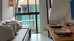 A modern room with a large window, a wooden dining table, a sofa, and a hanging light fixture. - Sunny Hall Flats  (Ipojuca)