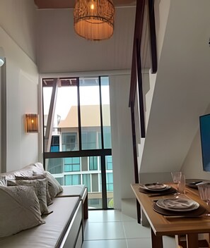A modern room with a large window, a wooden dining table, a sofa, and a hanging light fixture.